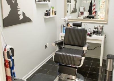 A hair cutting station with a black chair and a mirror at Details Salon & Spa
